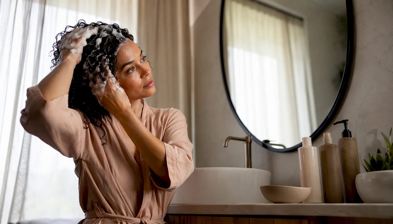 En kvinde står og vasker sit krøllede hår med shampoo.